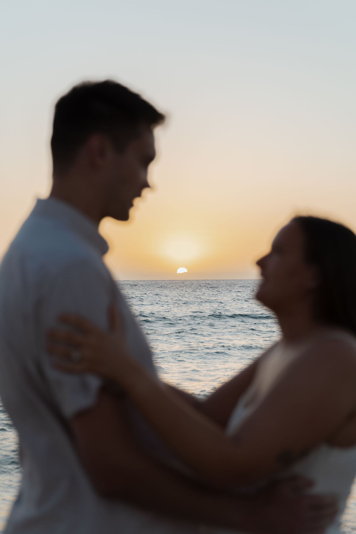 A couple embraces on the beach at sunset with ocean waves in background.