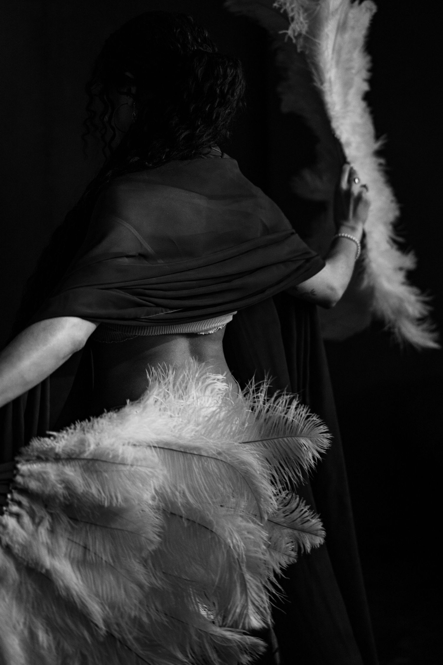 A dramatic black and white photo showing a figure with white feathers against a dark background.
