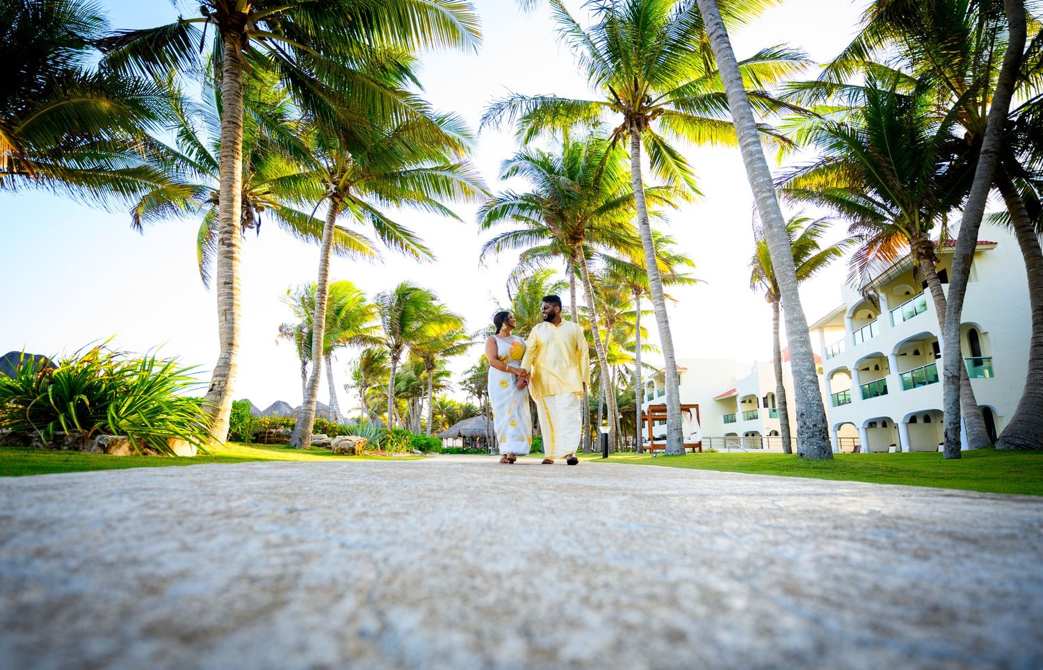 Couple walking through tropical palm trees at a resort during sunset.