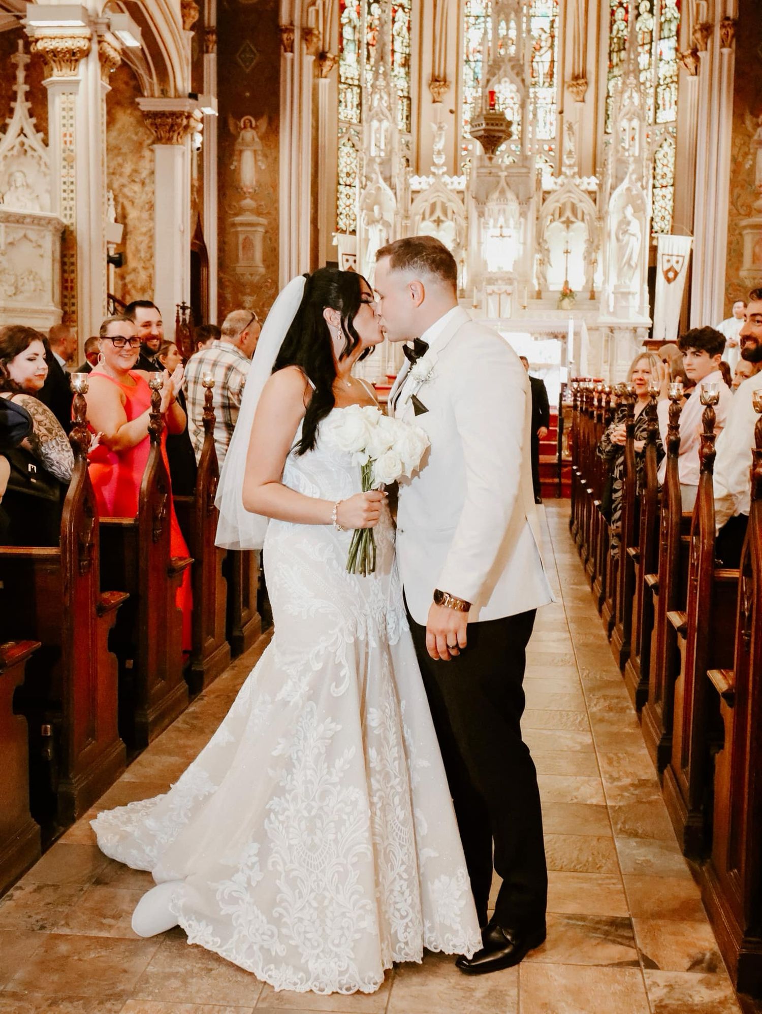 Newlywed couple holding hands while walking through wooden church doors, bride wearing lace train wedding dress.