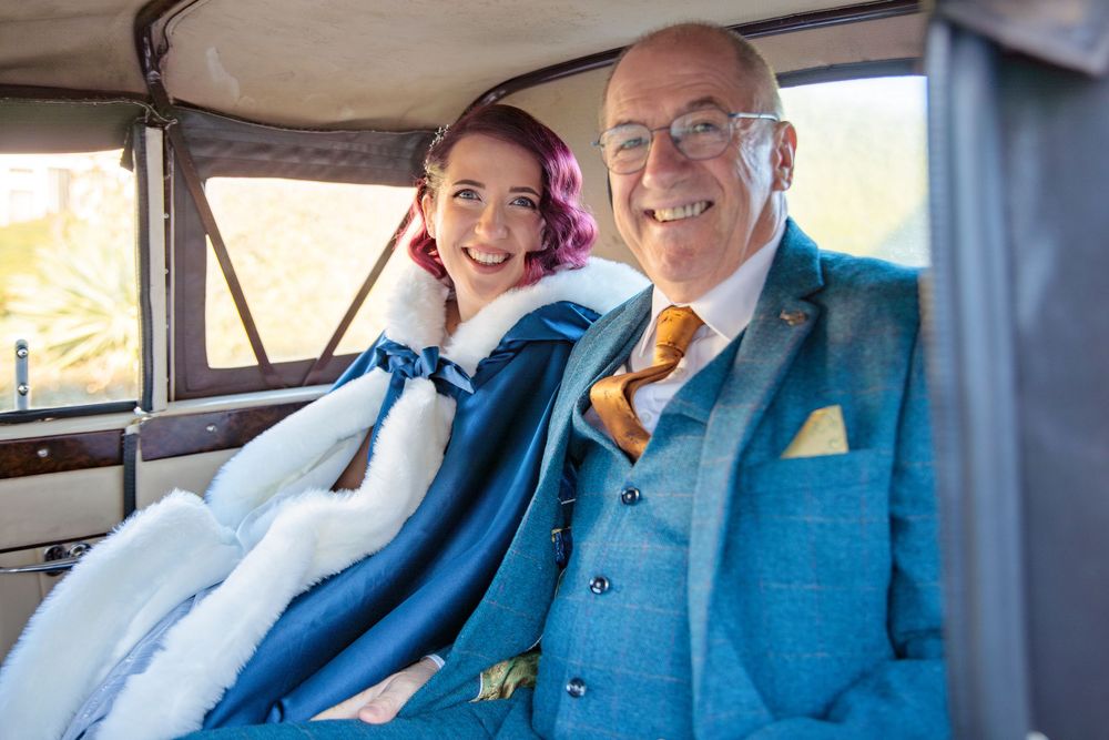 A happy couple sits together in a vintage car.