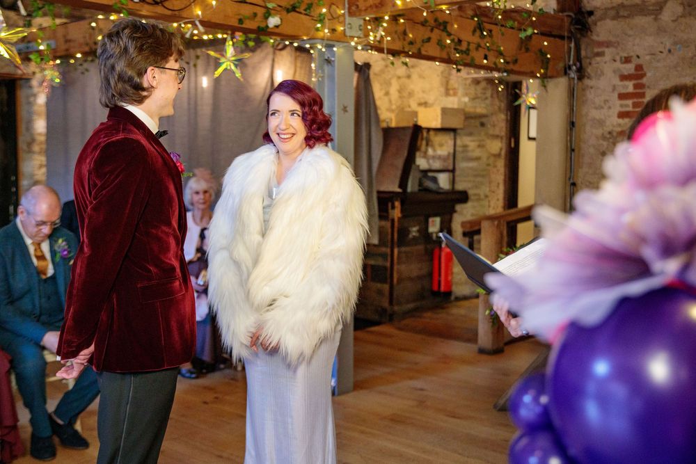 Wedding ceremony in rustic venue with purple balloon decorations.