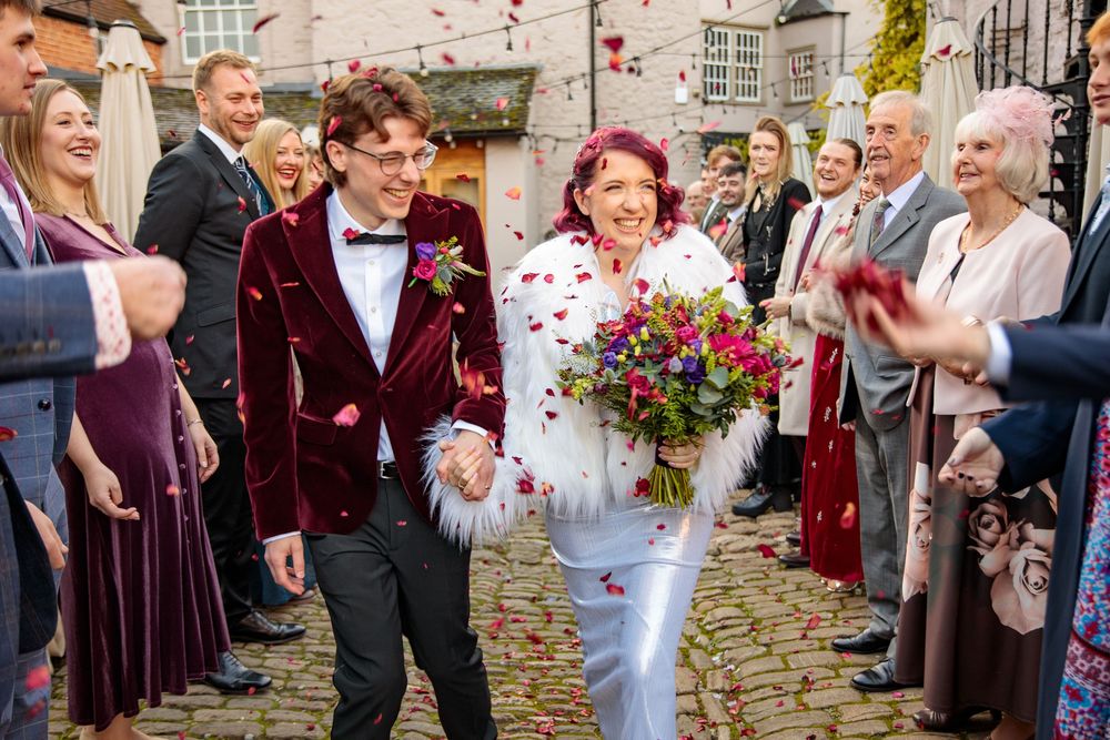 Wedding couple walks through shower of confetti while guests cheer.