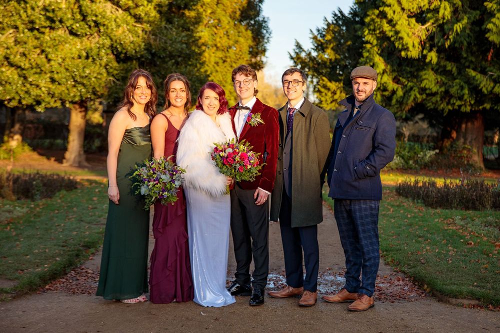 Wedding party in formal attire poses outdoors with autumn foliage in background.