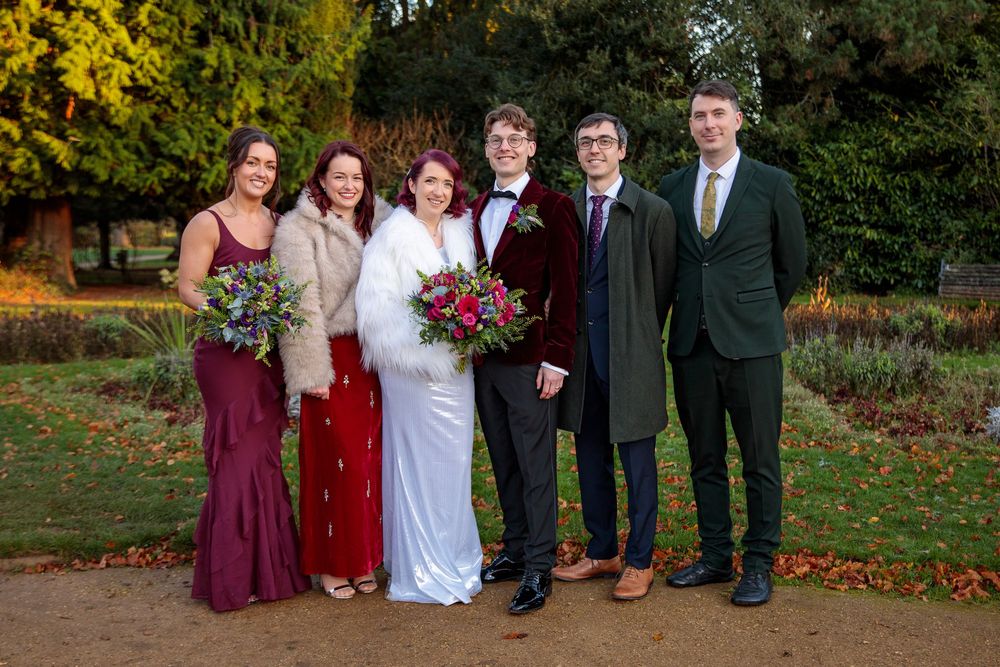 Wedding group photo with burgundy and green color scheme against fall outdoor backdrop.