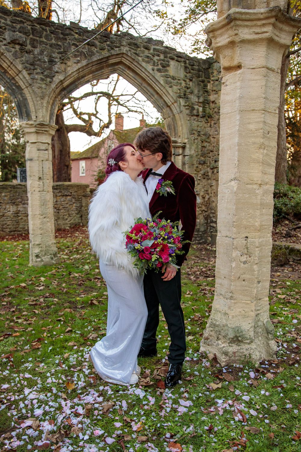 Couple shares romantic moment under stone archway surrounded by fallen leaves.