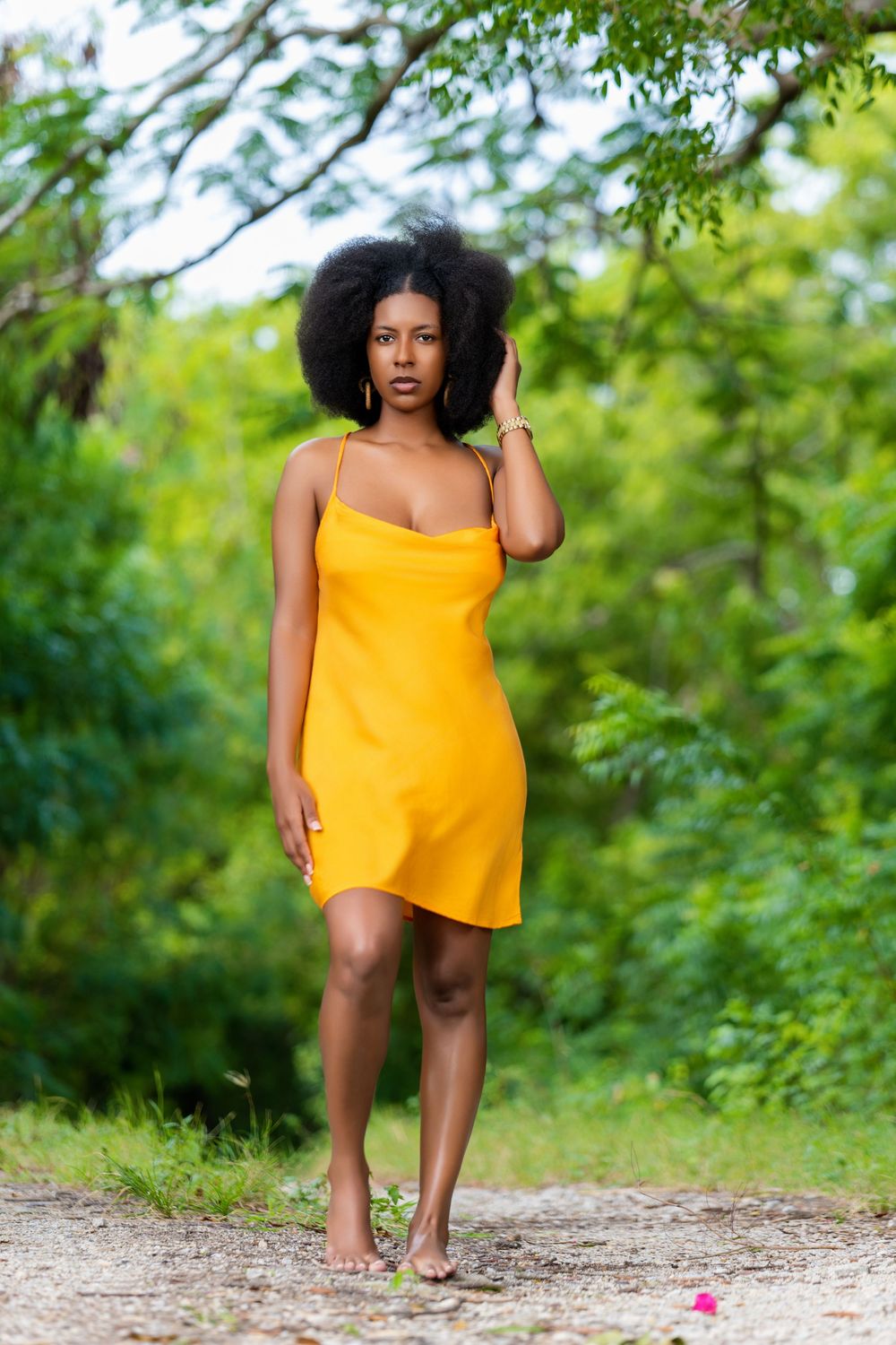 Woman wearing a yellow sundress poses on a nature path surrounded by lush greenery.