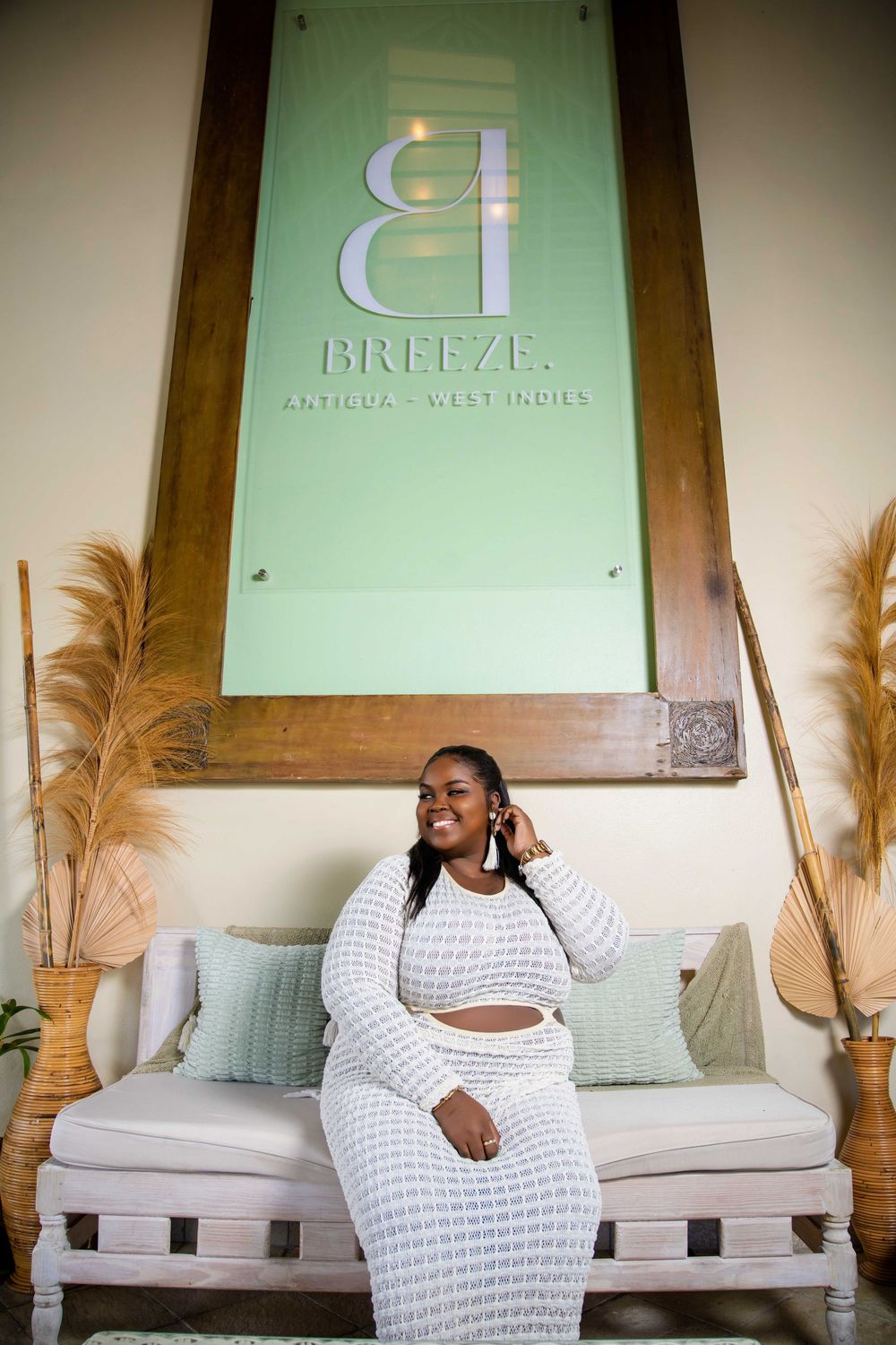 Person in white crochet outfit poses on couch under Breeze Antigua resort sign.