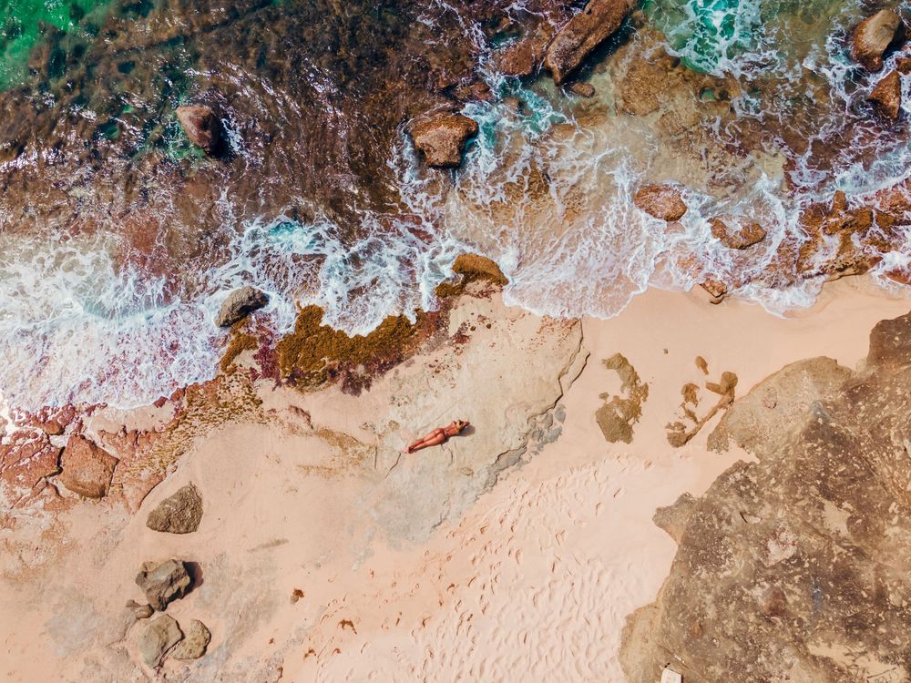 Aerial view of ocean waves crashing on sandy beach with rocky coastline.