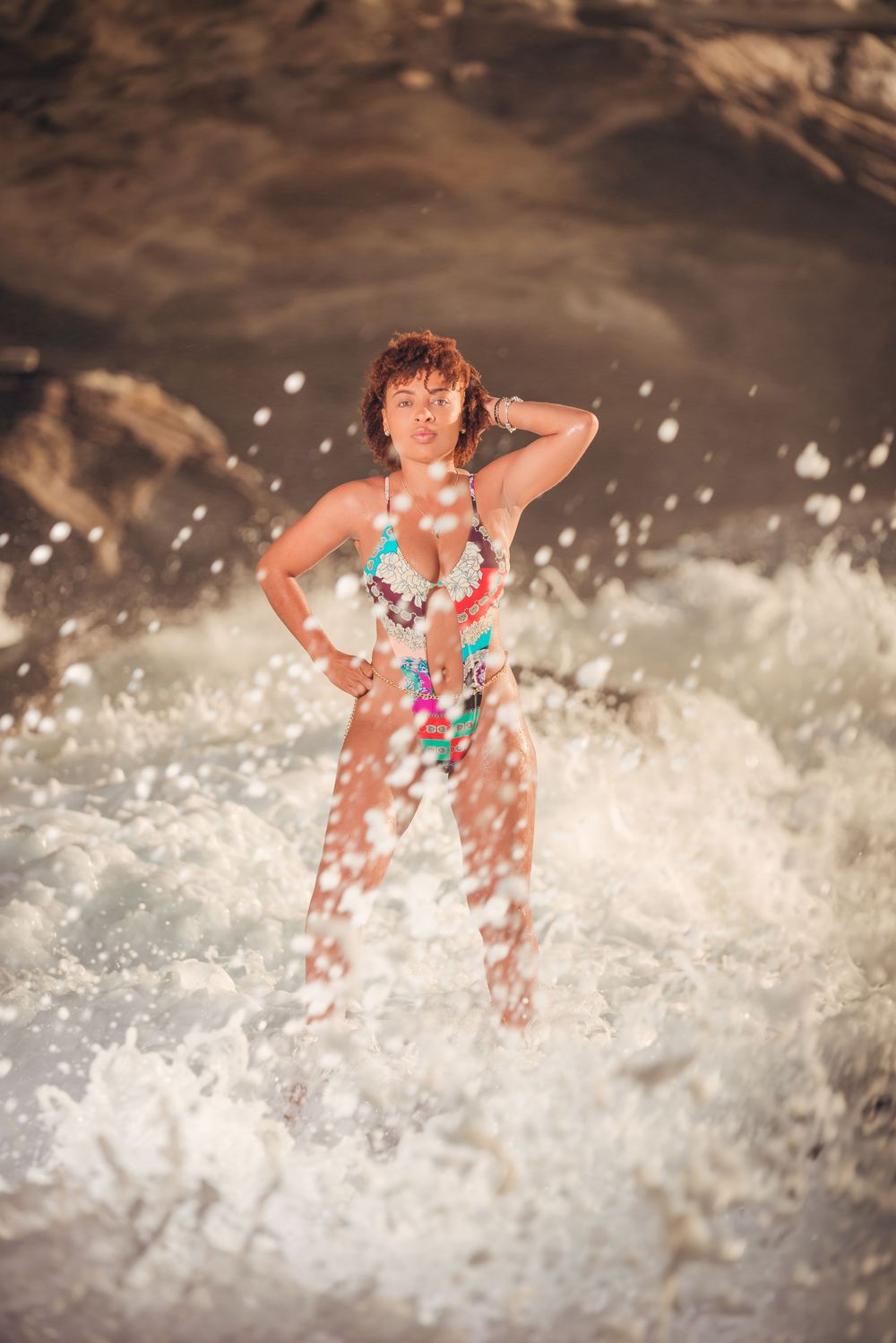 Figure stands in crashing ocean waves wearing floral swimsuit.