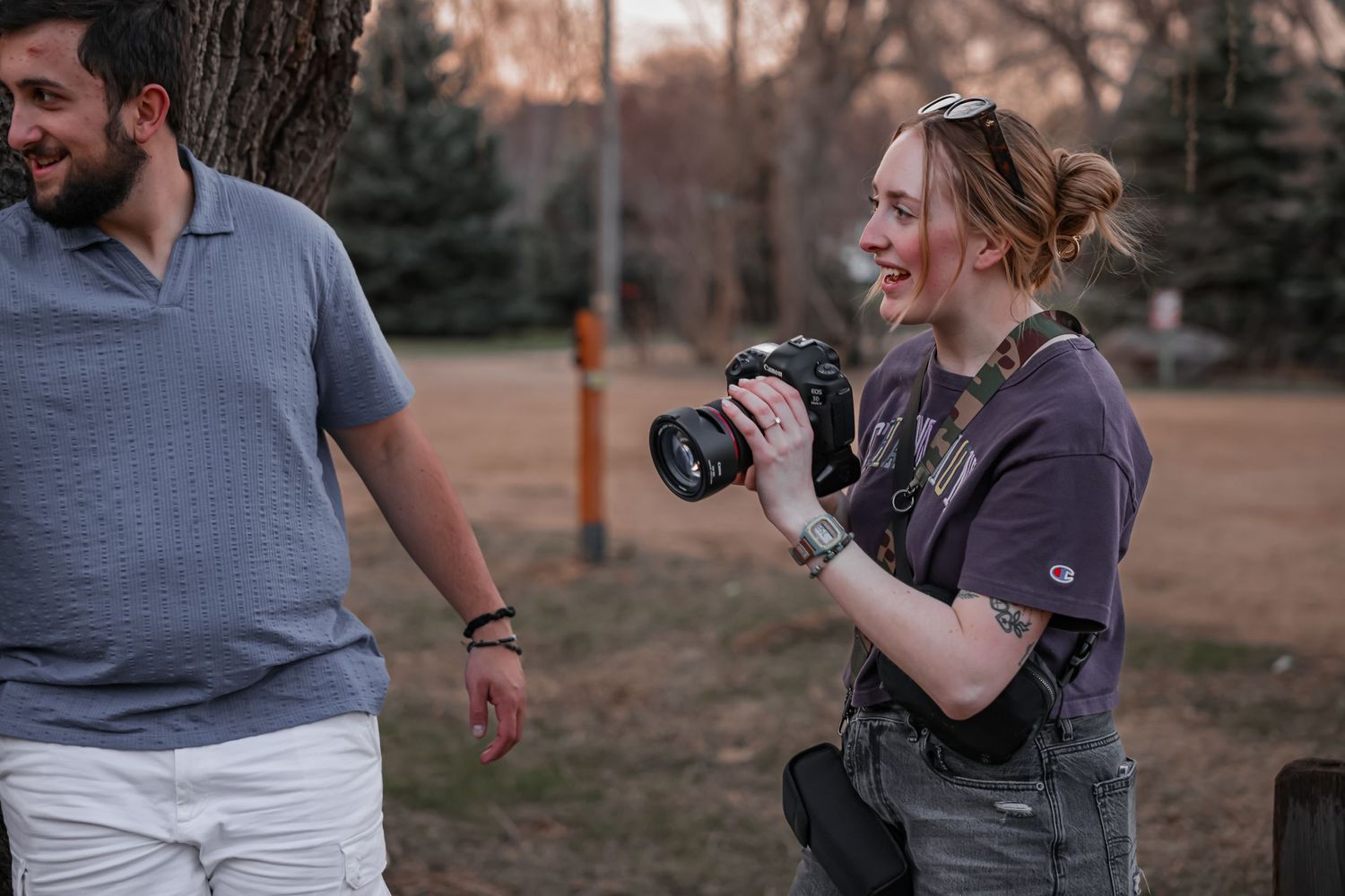 A photographer with a camera kneels while taking pictures outdoors at dusk.