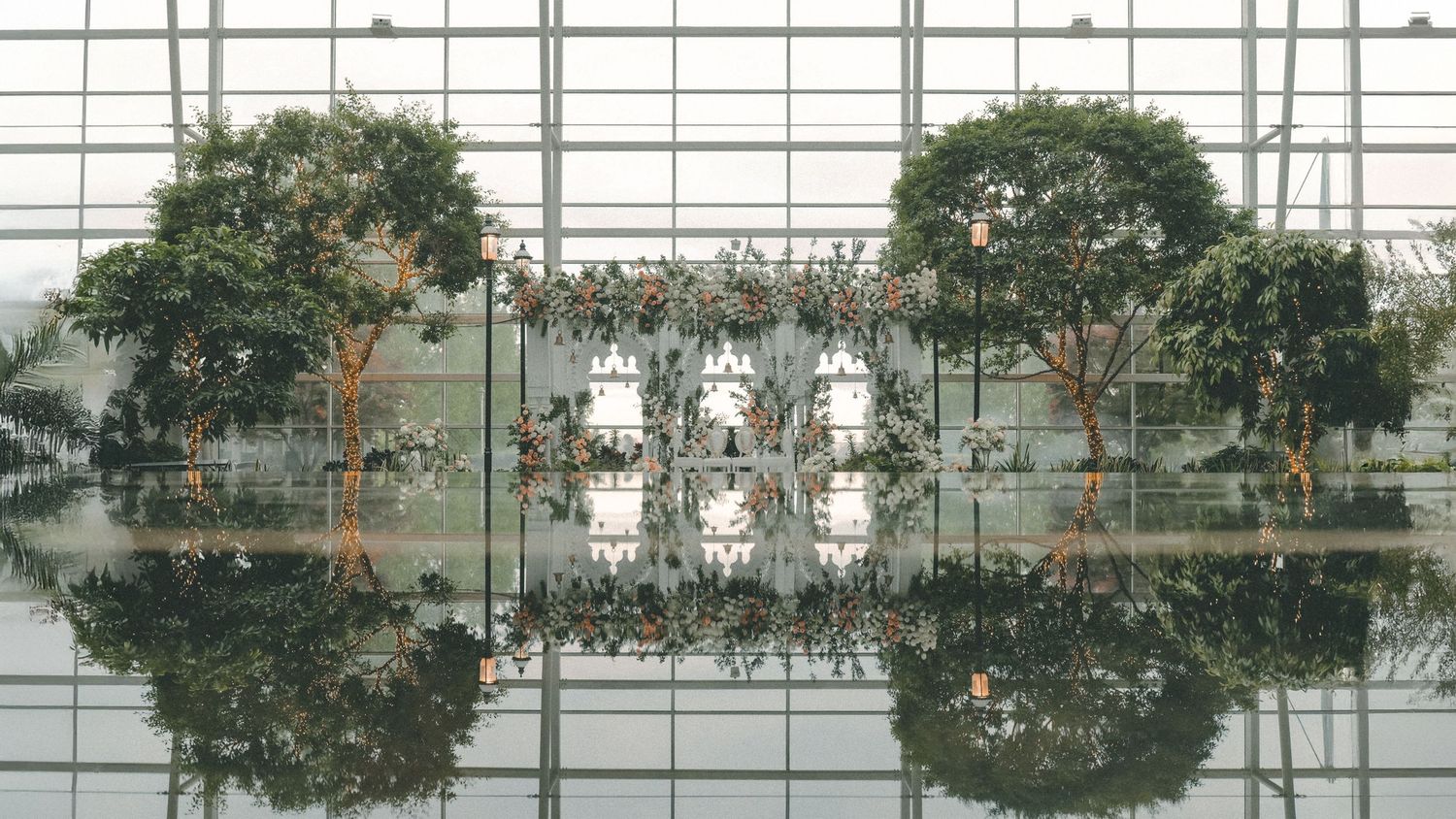 Modern glass atrium with trees creating perfect symmetrical reflection in still water.