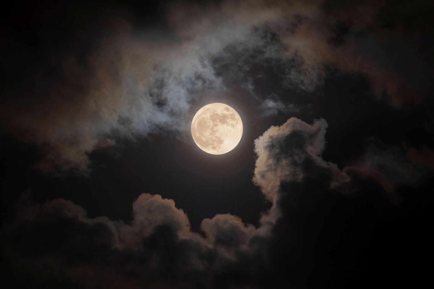 Bright full moon framed by dramatic clouds in a dark night sky, with light halos illuminating the surrounding mist.