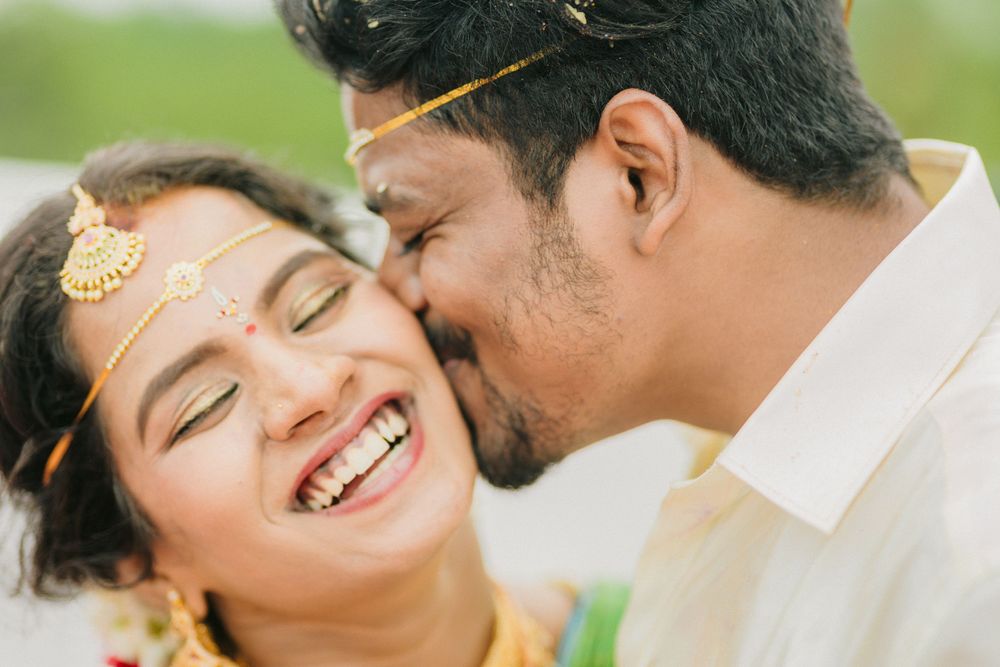 A couple shares a joyful tender moment outdoors while wearing traditional Indian wedding attire.