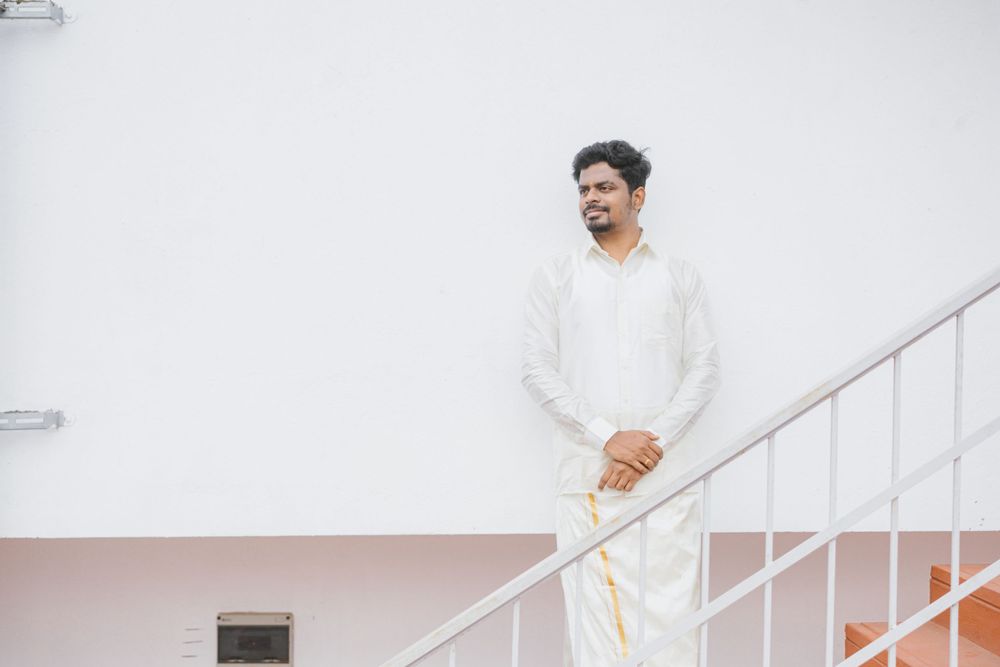 A minimal portrait on white stairs showing a person in traditional white Indian formal wear.
