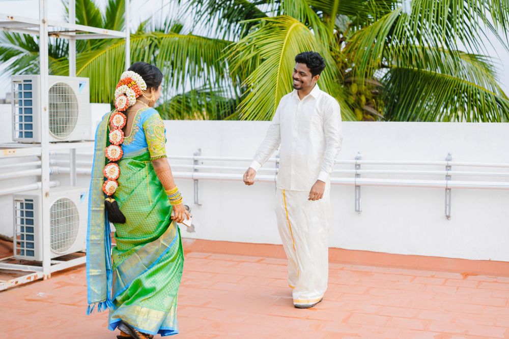 Two individuals in traditional South Asian attire smile while spending time together on a rooftop terrace with palm trees.