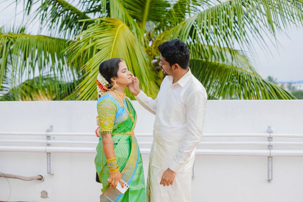 Couple in traditional Indian attire sharing playful moment on white balcony with tropical backdrop.