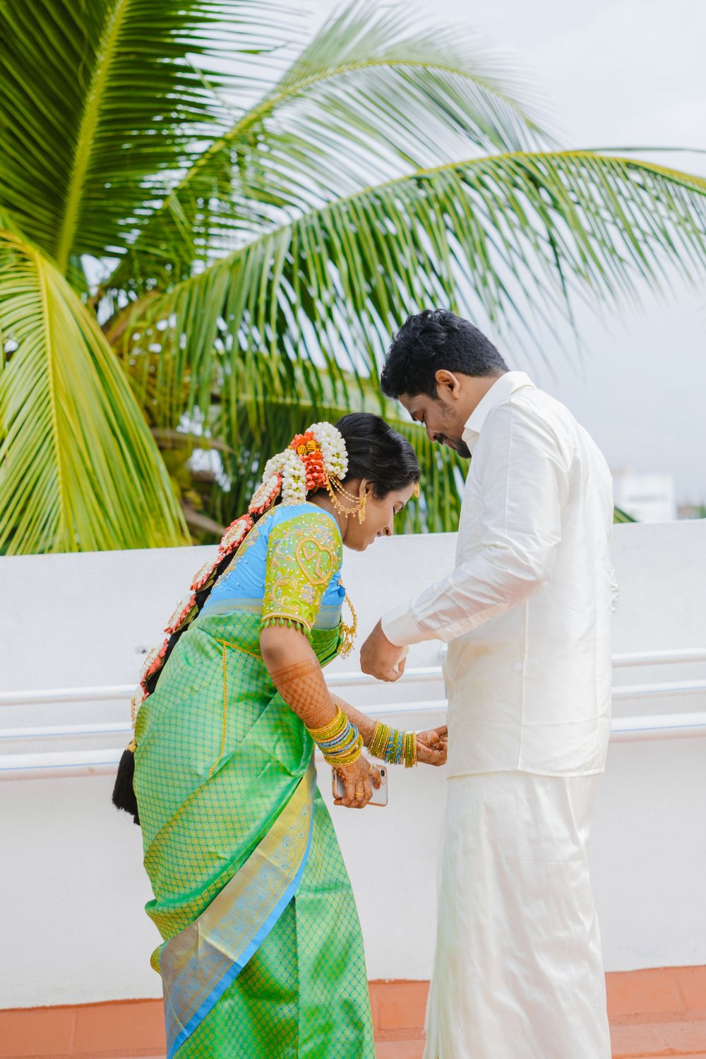 Traditional South Indian couple performing wedding rituals against palm tree backdrop.