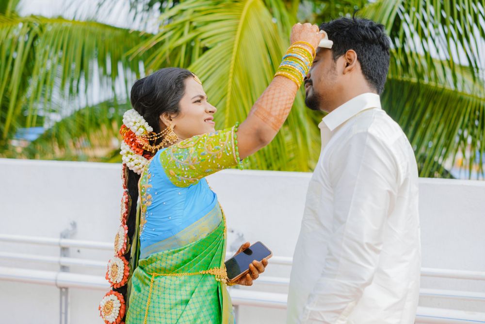Traditional ceremony with woman placing tikka on forehead against palm tree backdrop.