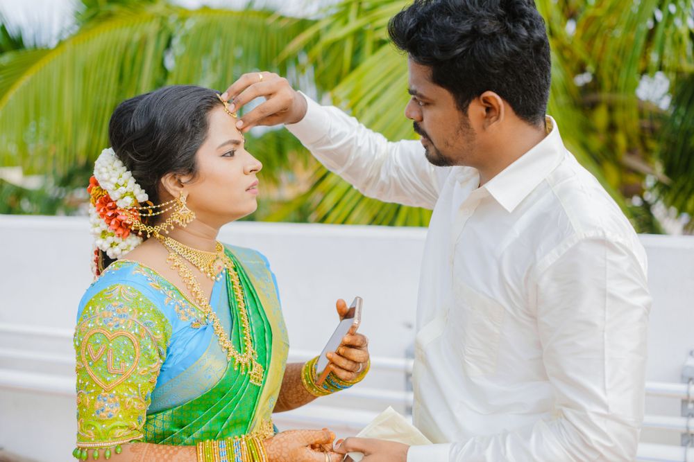 A couple in traditional Indian attire shares a sweet moment during a ceremony against a tropical backdrop with palm trees.