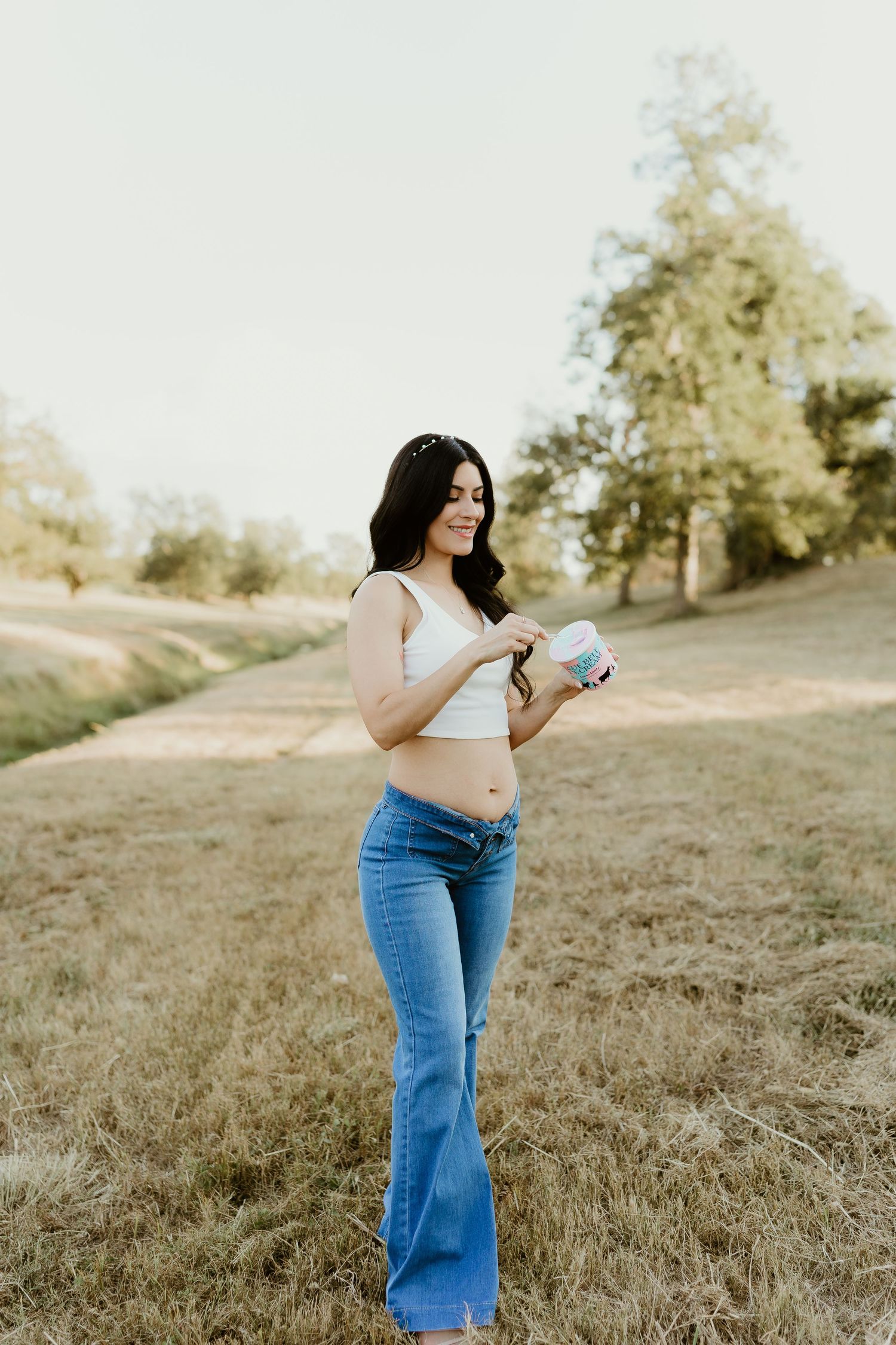 Woman in jeans poses in a grassy field during golden hour photoshoot.