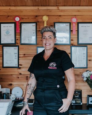 A professional in a black uniform stands in front of certificates on a wooden wall in a business setting.