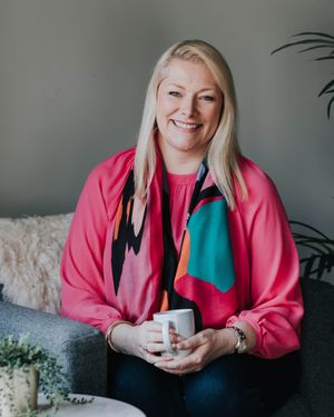 A person wearing a bright pink sweater sits comfortably on a couch with a mug.