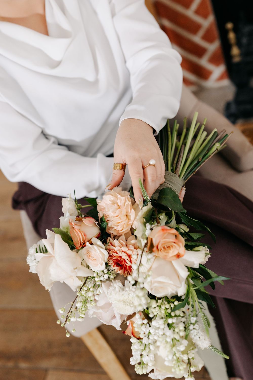 Hands in white sleeves arrange delicate peach roses and baby's breath flowers into a romantic wedding bouquet.