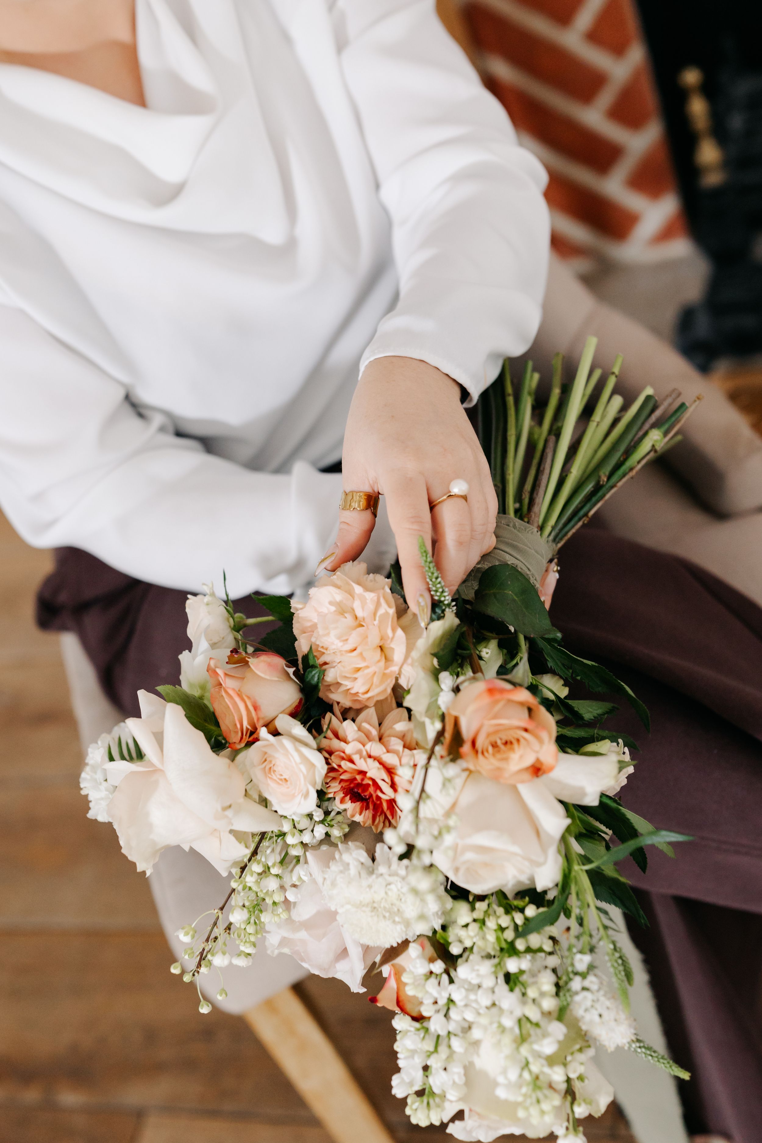 Hands in white sleeves arrange delicate peach roses and baby's breath flowers into a romantic wedding bouquet.