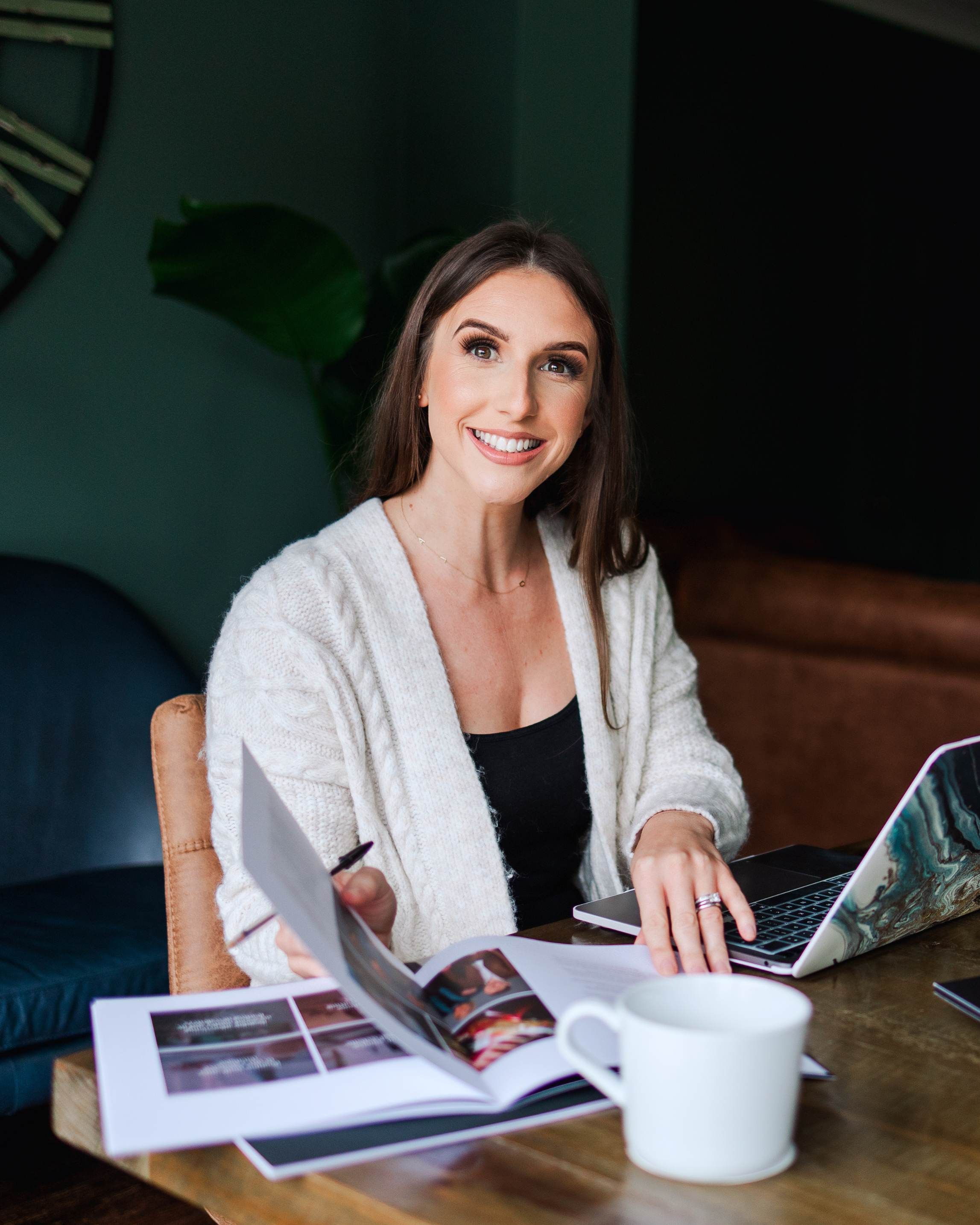Person working at wooden table with laptop and papers in modern interior setting.