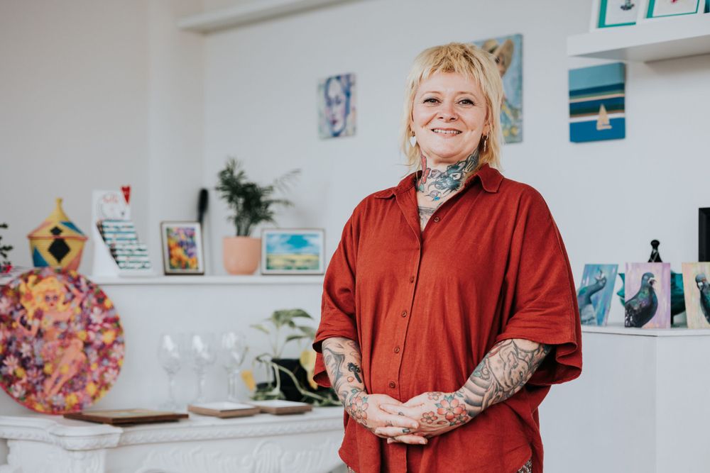 A chef in a red button-down shirt with visible tattoos stands smiling in a bright white kitchen.