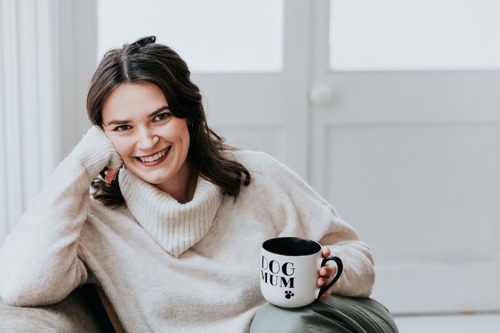 Someone in a cozy cream turtleneck sweater relaxes at home with a coffee mug and warm smile.
