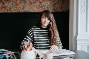 Focused student in striped sweater reading textbook at desk with long curly hair and soft natural lighting.