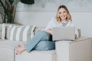 A casual scene shows someone working on a laptop while relaxing comfortably on a beige couch with striped pillows.