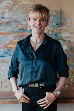 Professional portrait of someone in a navy button-down shirt and jeans standing in front of abstract wall art.