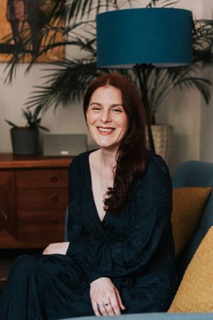A joyful portrait in an interior setting with a teal lampshade, dark dress, and houseplants visible in the background.