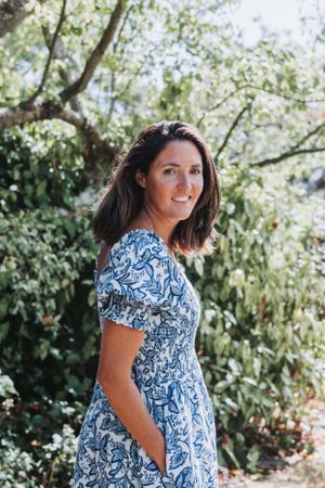 Someone wearing a blue and white floral print dress poses outdoors near blooming trees on a sunny day.