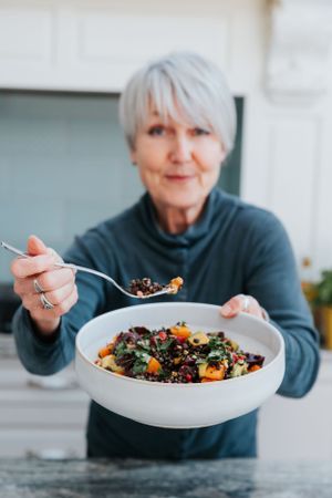 Person in a navy sweater enjoying a healthy grain bowl with colorful vegetables and toppings.