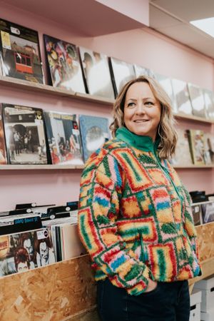 Person wearing colorful patterned fleece sweater browses vinyl records in music store with pink walls.