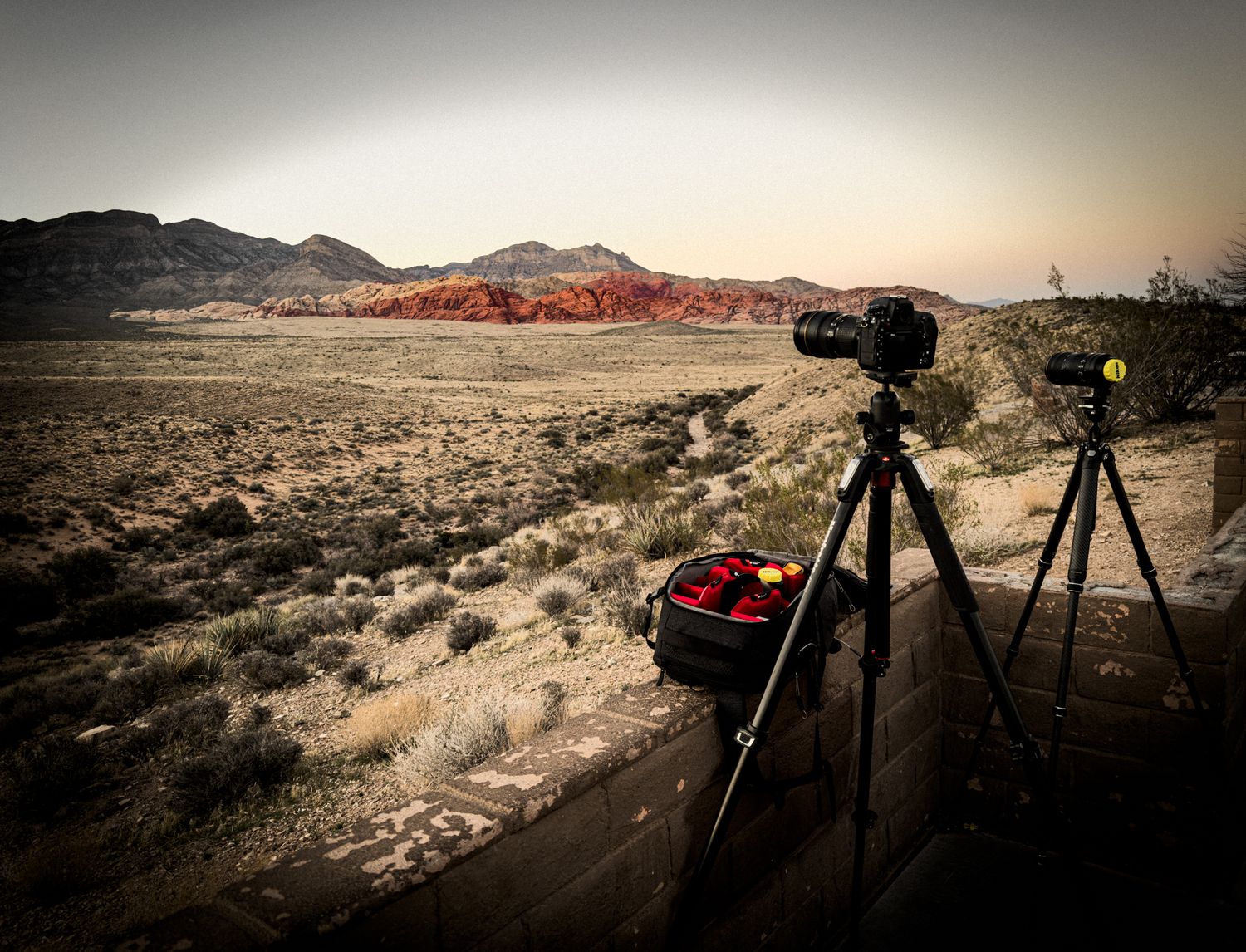 Desert landscape photography equipment silhouetted against dramatic sunset mountains.
