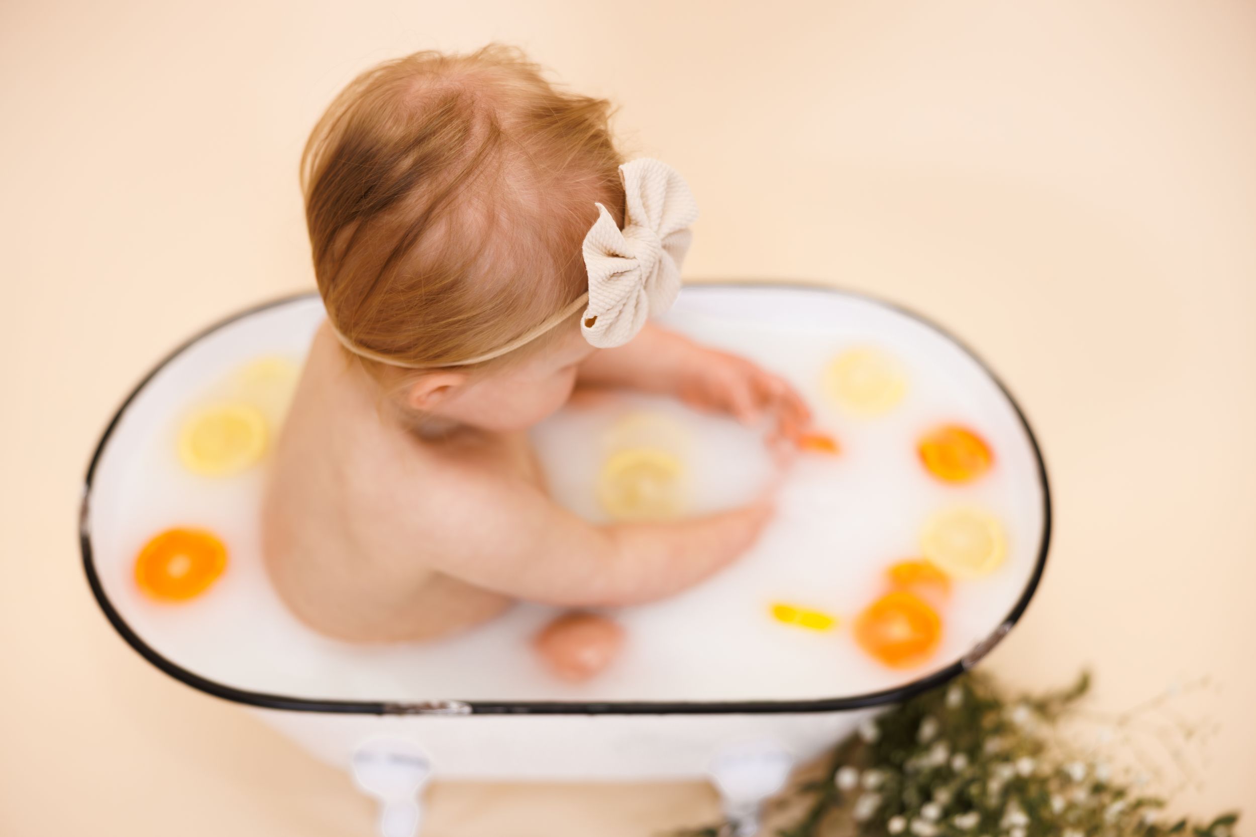 Overhead view of a baby taking a bath in a white tub with orange bath toys and bubbles.