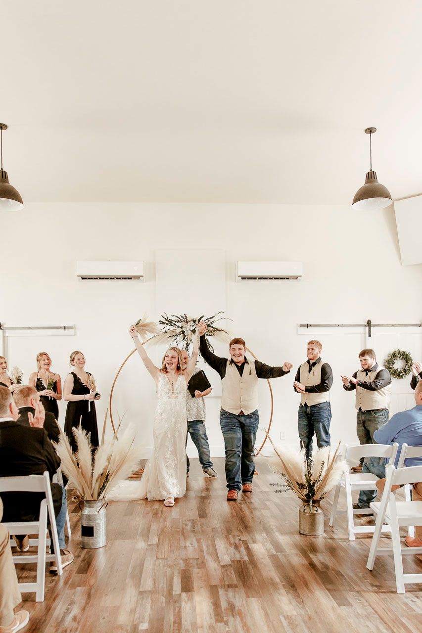 Couple celebrates their wedding ceremony in a modern white venue with arch decorated with pampas grass and pendant lights.