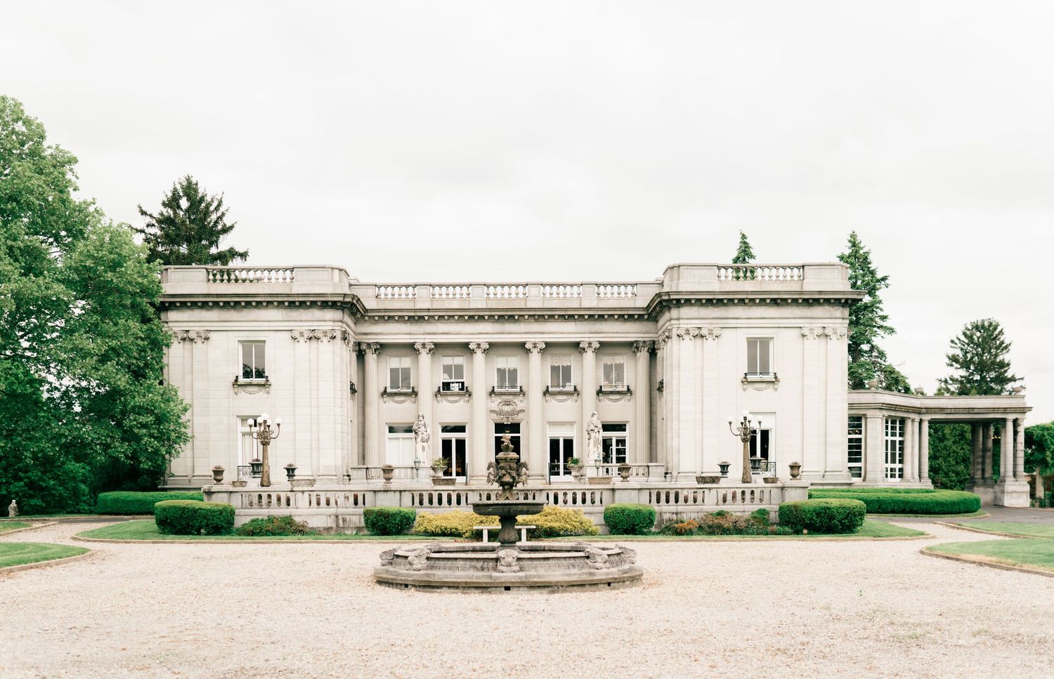 A couple stands on grand stone steps of an elegant neoclassical building with white columns and architectural details.