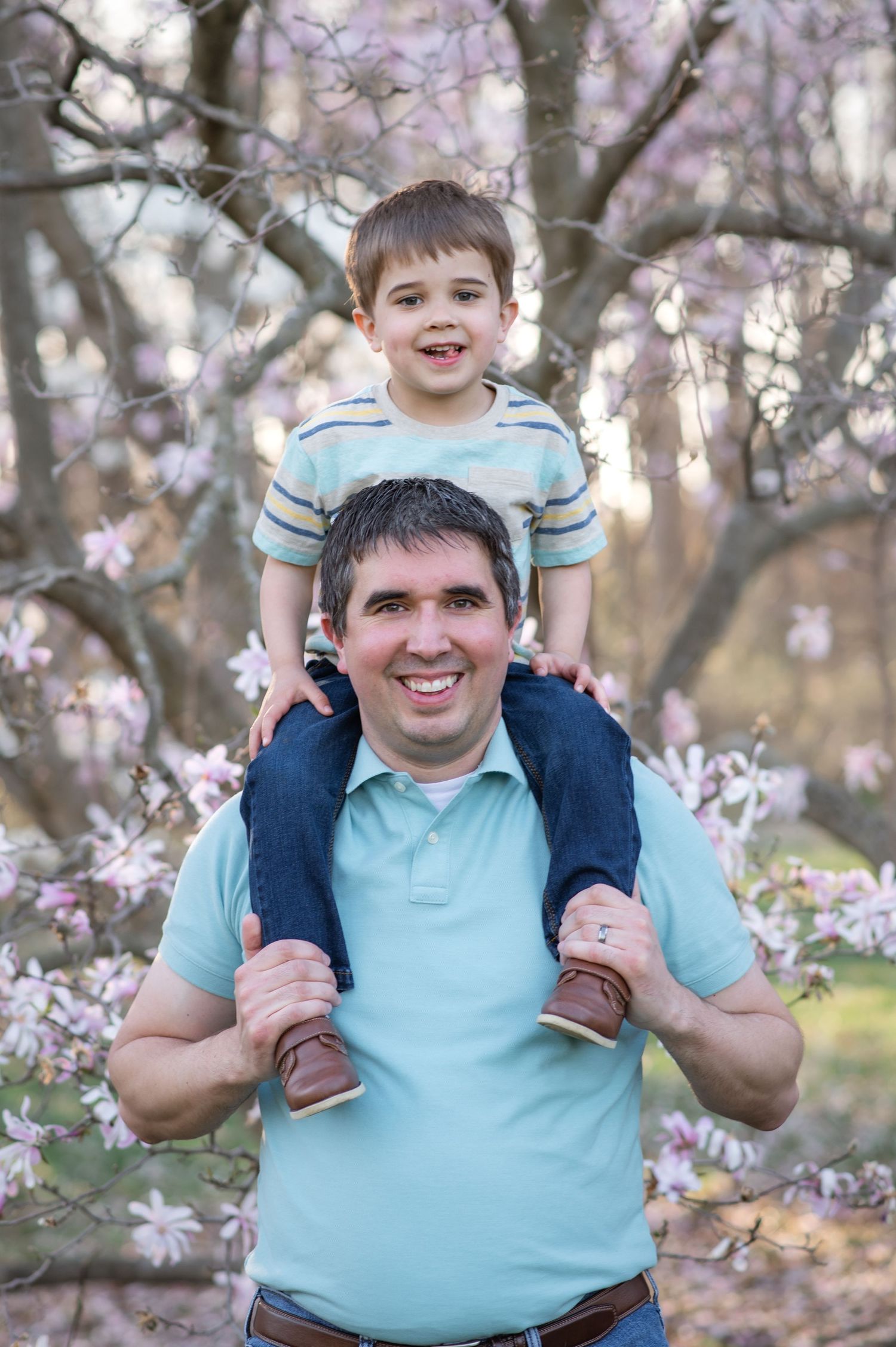 Parent and child posing together in front of blooming magnolia trees during springtime photo session.