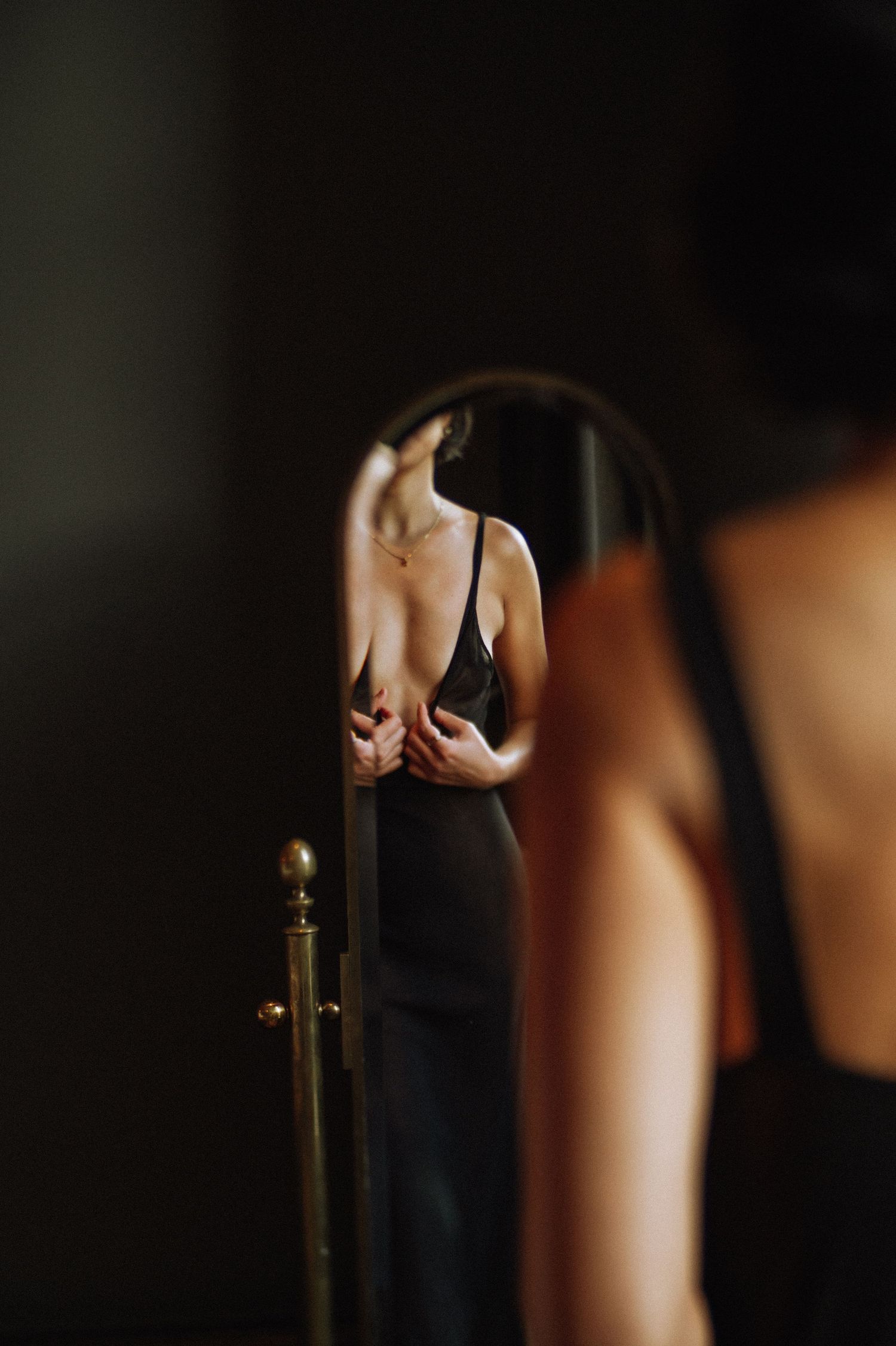Reflection in the mirror – a woman gazes softly at her body during an introspective boudoir photoshoot.
