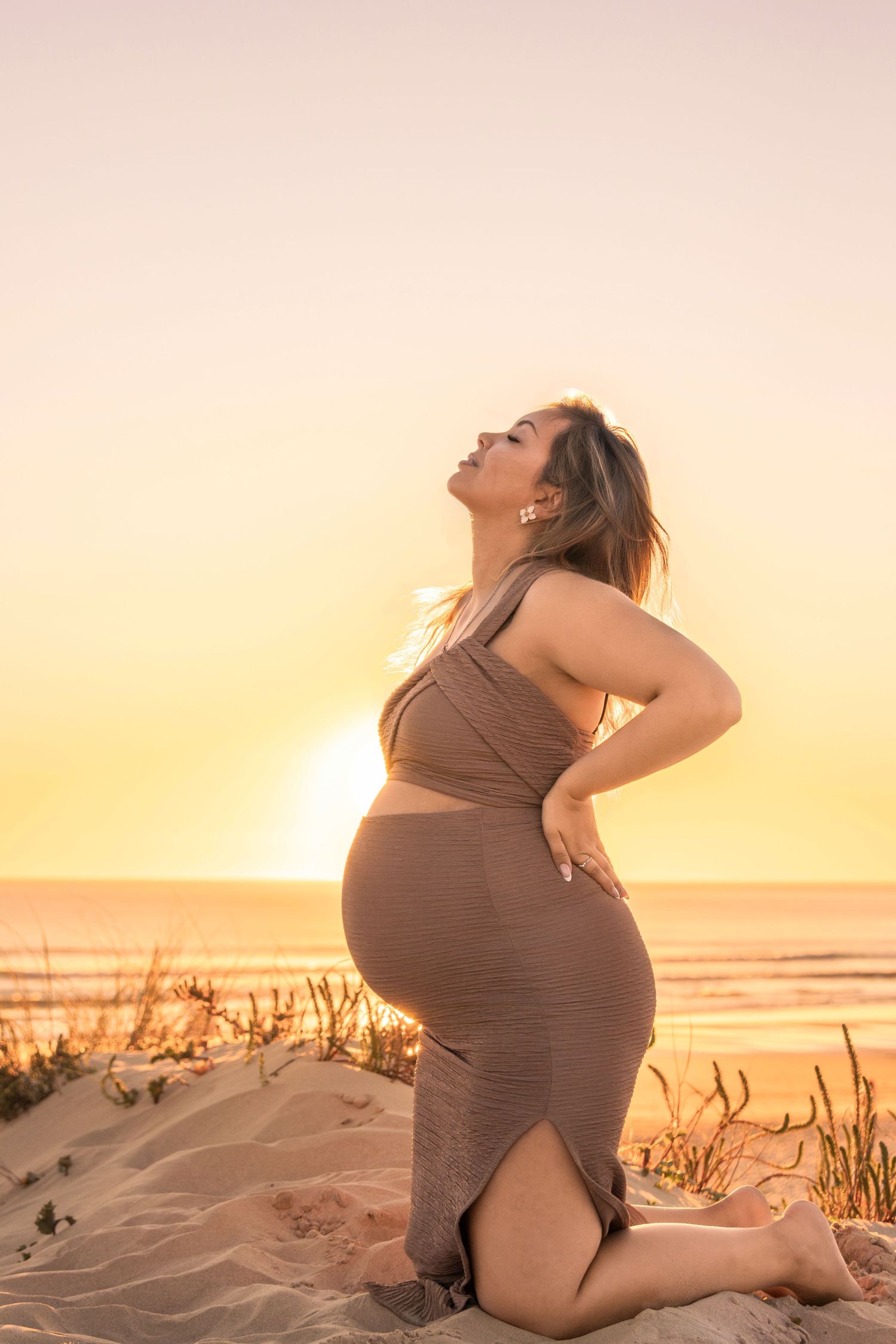 Maternity photoshoot at sunset on a sandy beach with warm golden lighting.