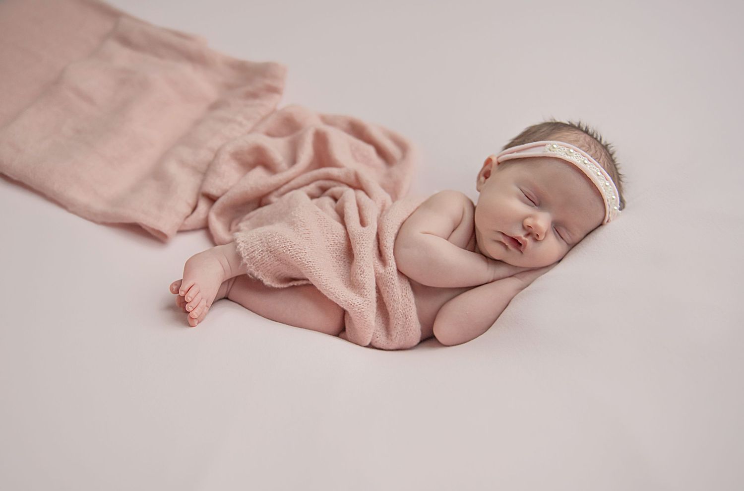 Sleeping newborn baby wrapped in soft pink blanket during professional photo session.