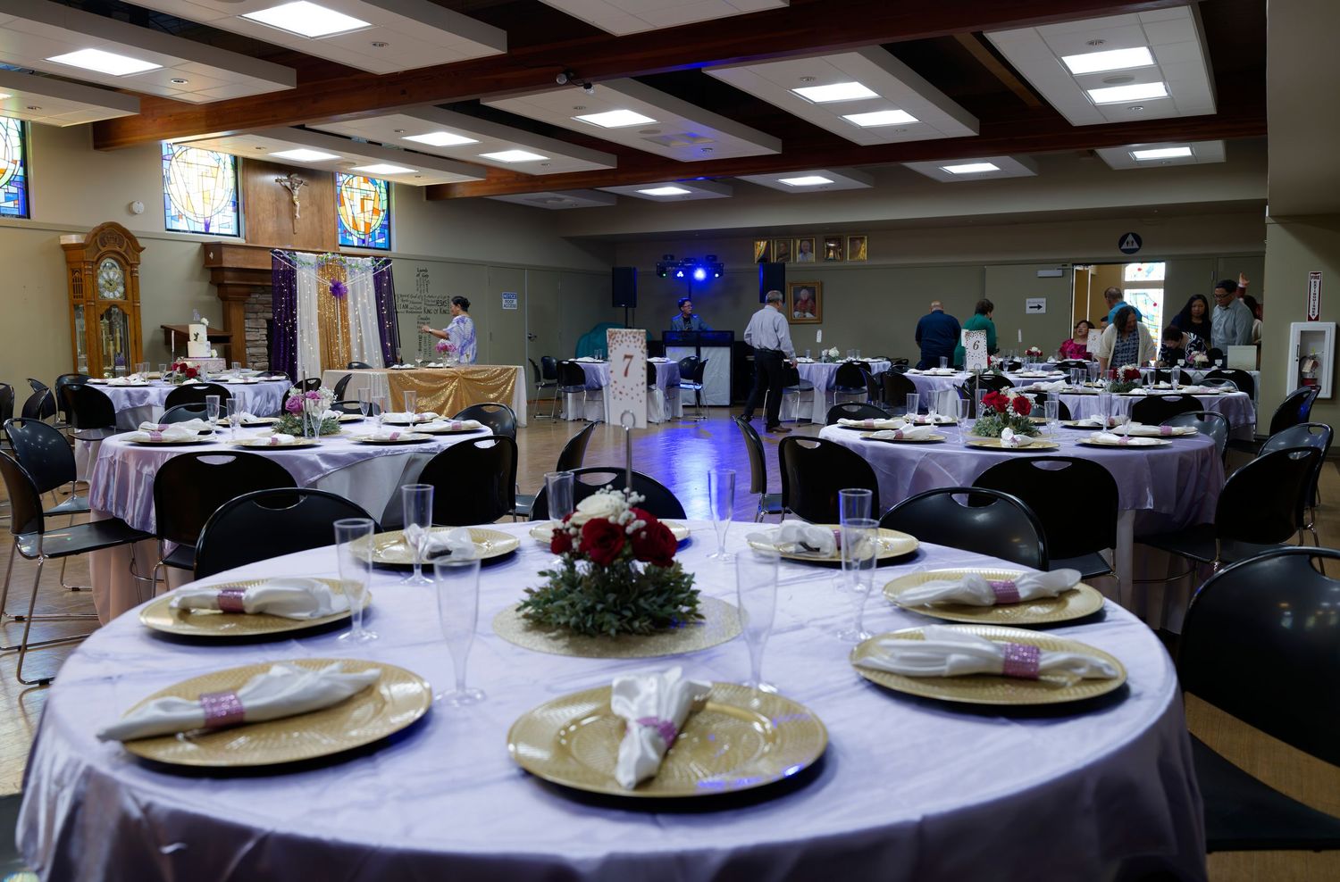Round tables with white tablecloths set for formal dining in a banquet hall with overhead lighting and floral centerpieces.