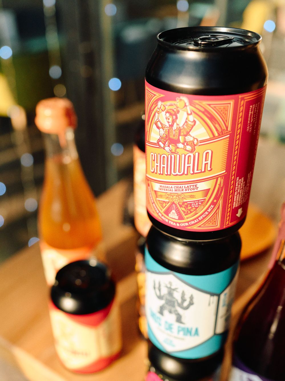 Close-up photo of colorful craft beer cans stacked on a wooden surface with blurred background lighting.