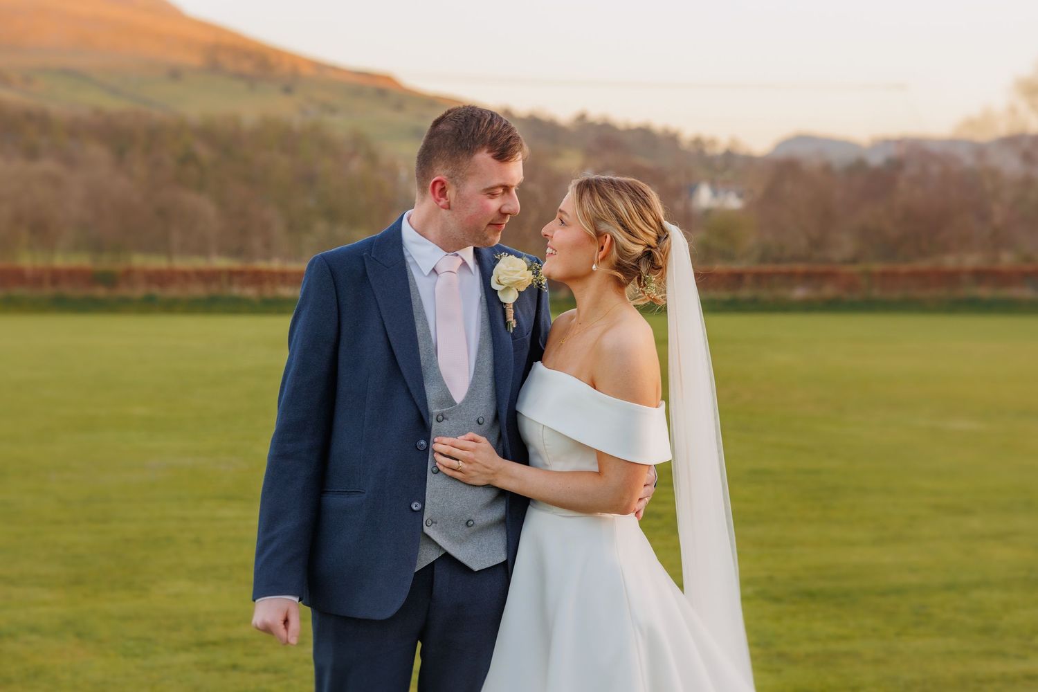 A tender wedding portrait of a couple on a green lawn with countryside hills in the background.